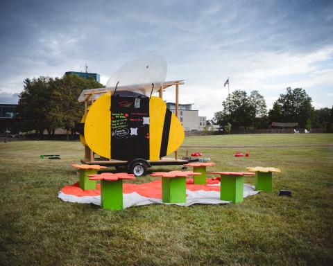 A black and yellow sculptural bee sits on a lawn.